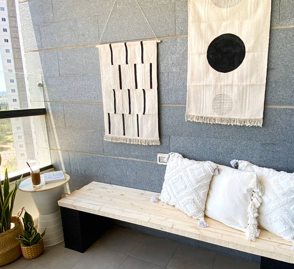 מבט לכיוון קיר המרפסת הכולל את שלושת פרויקטי ה־DIY: שולחן קפה, שטיחים צבועים וספסל ישיבה